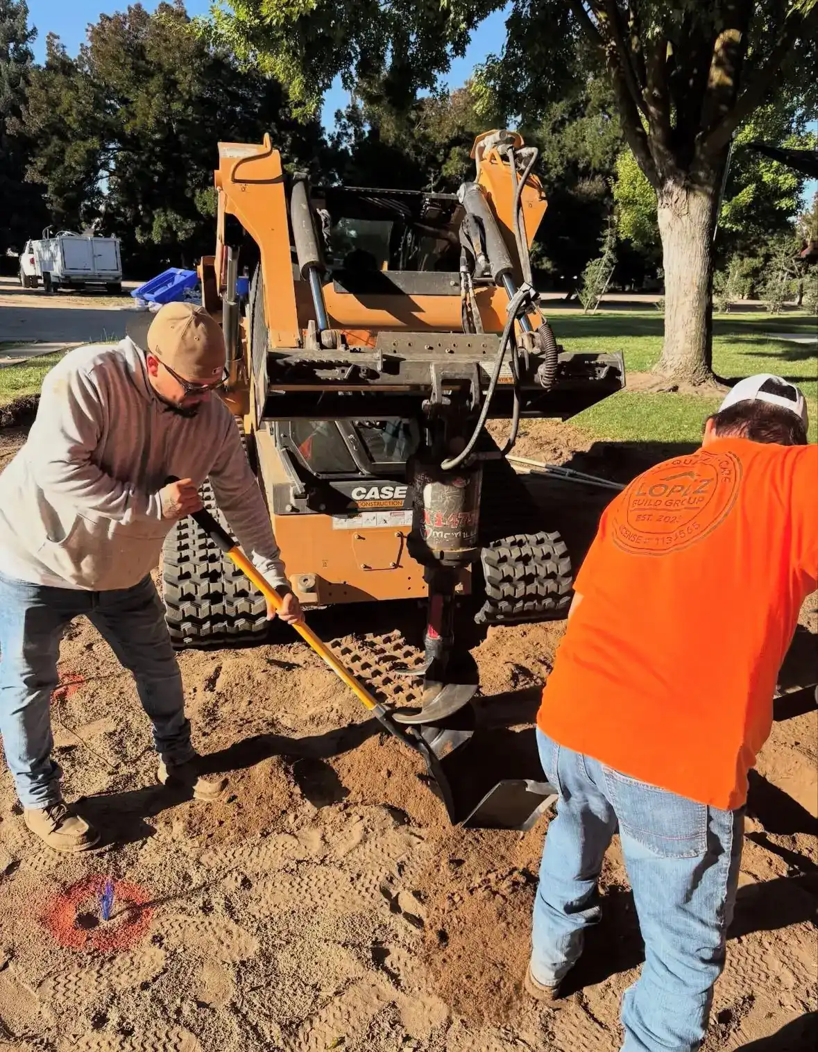 Two Lopez crew members drilling footings with a tracked loader and auger
