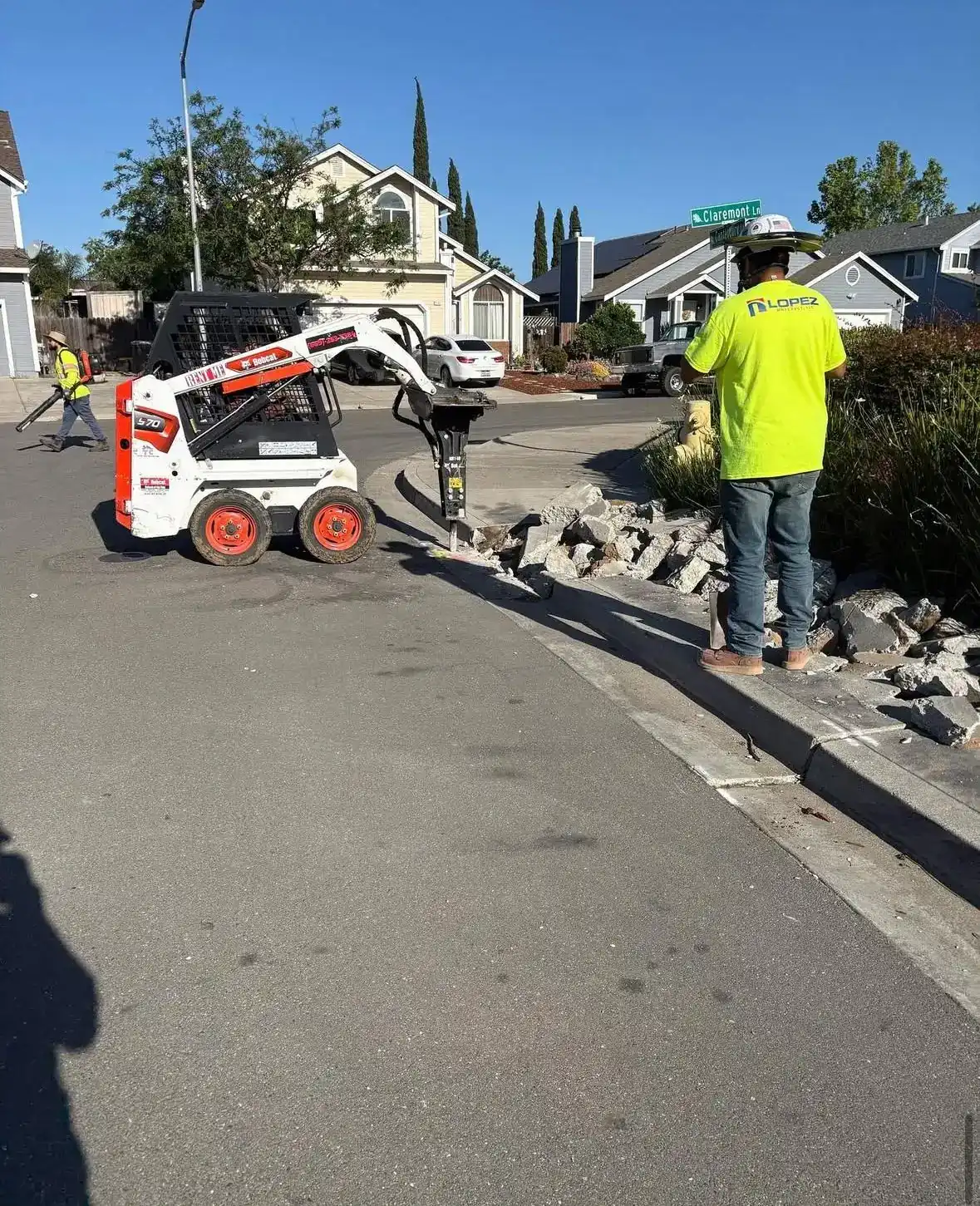 Skid steer breaking out an old curb while a Lopez foreman watches the street