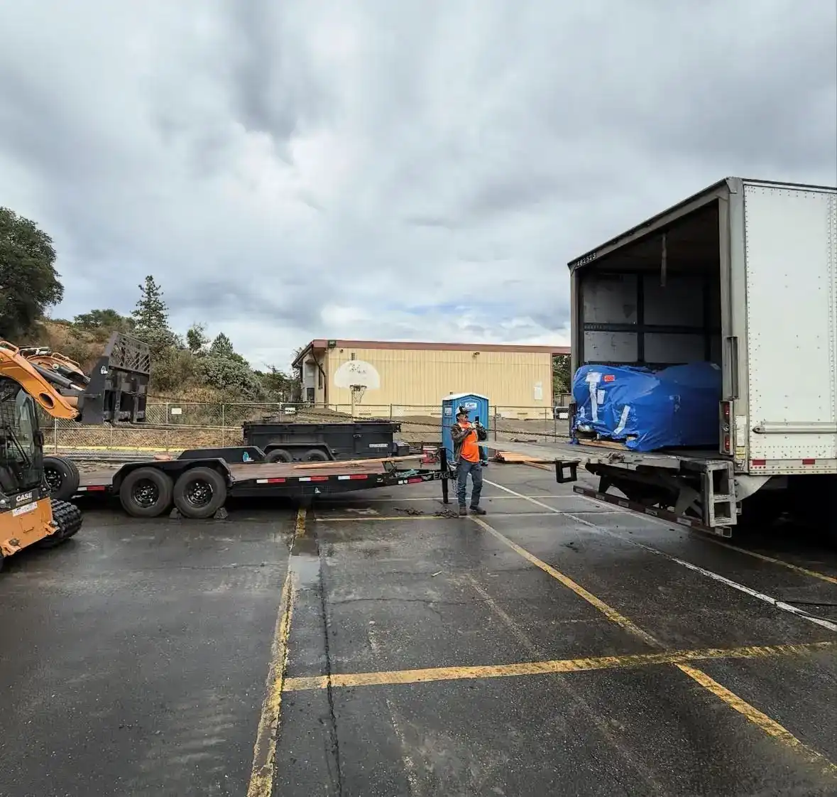 Equipment trailer and box truck staged in a school parking lot