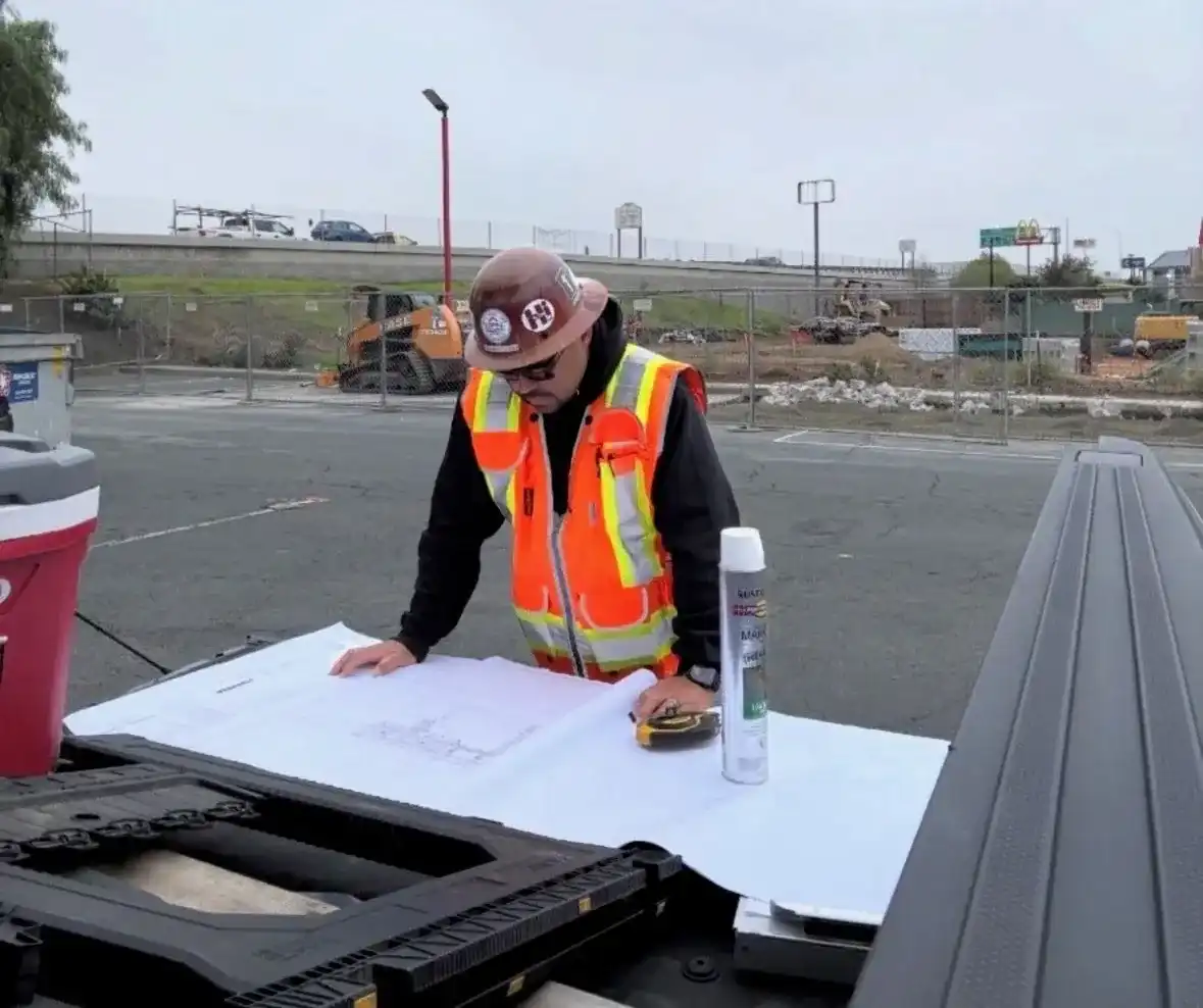 Lopez foreman in a hard hat and safety vest reviewing site plans on a truck tailgate at an active jobsite