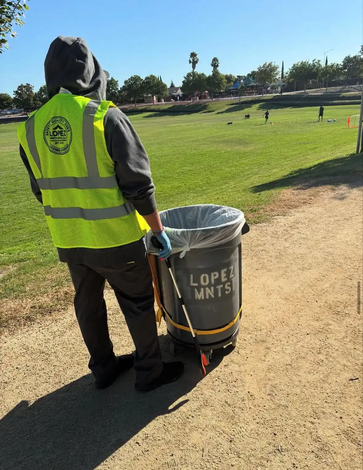 Crew member servicing a park trash can on a sports field
