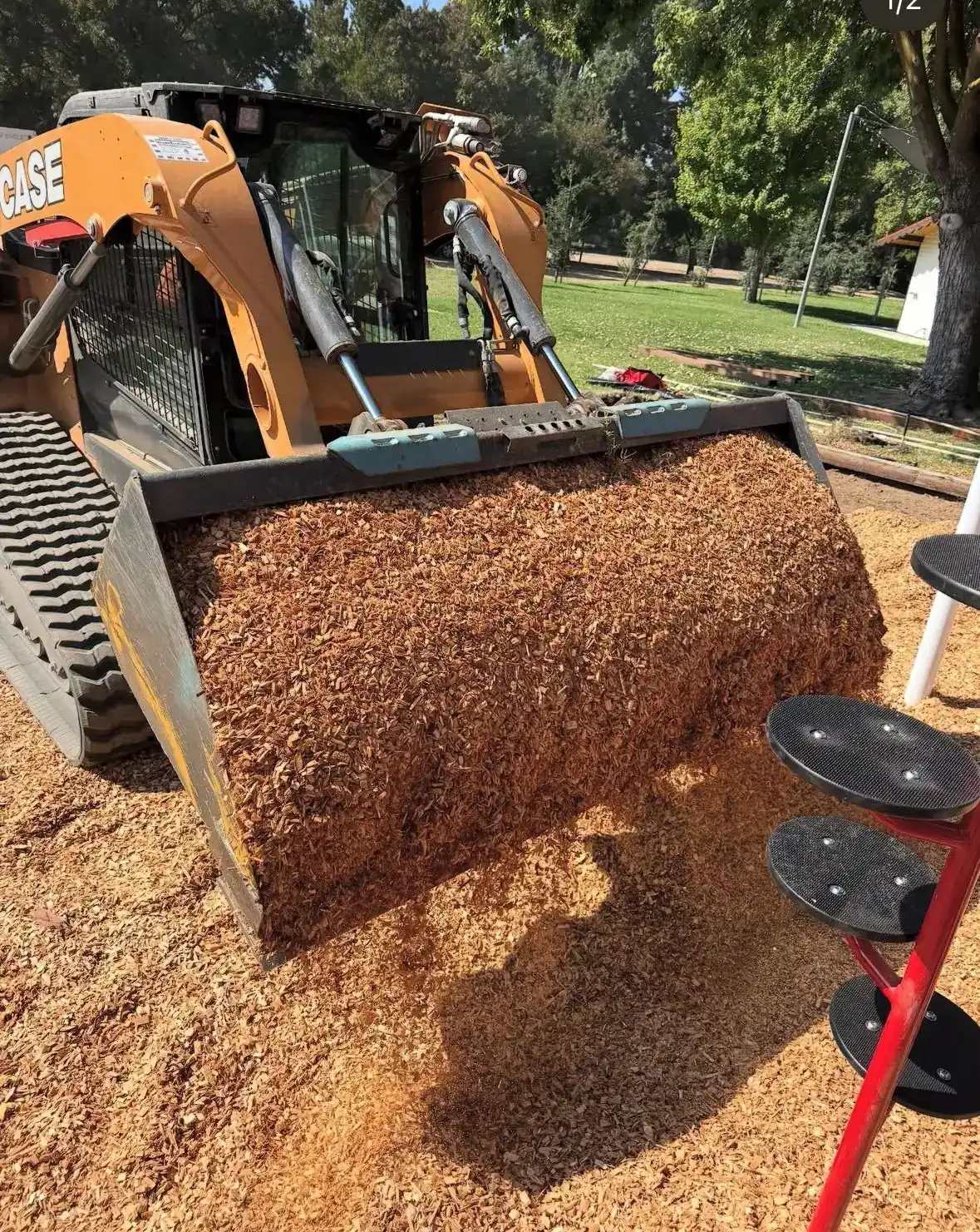 Loader bucket of wood fiber surfacing at a playground install