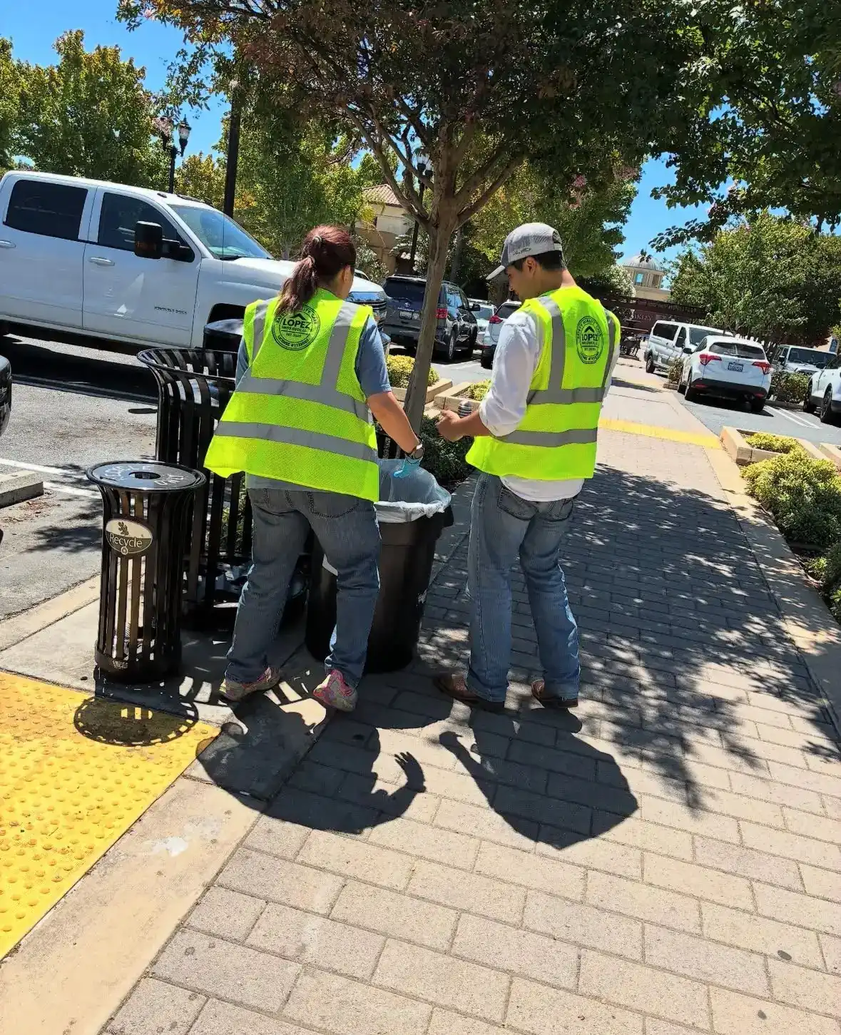 Two crew members servicing trash receptacles along a downtown sidewalk