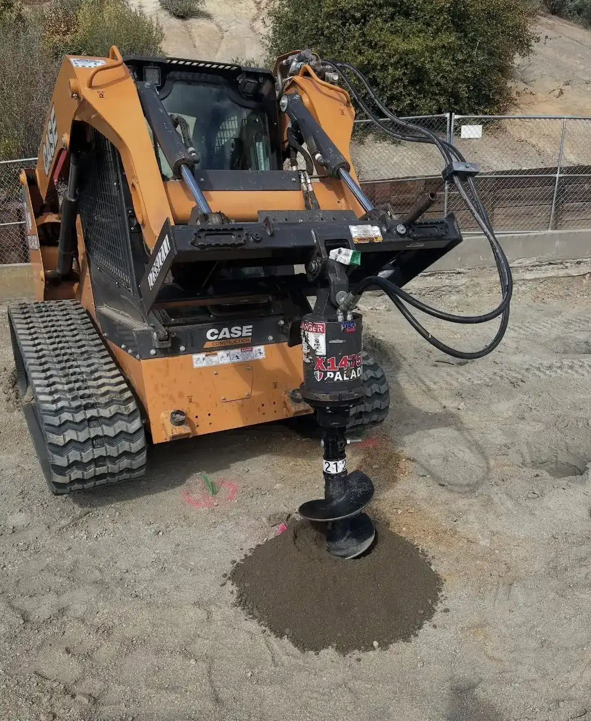 Tracked loader with an auger attachment staged on a graded site