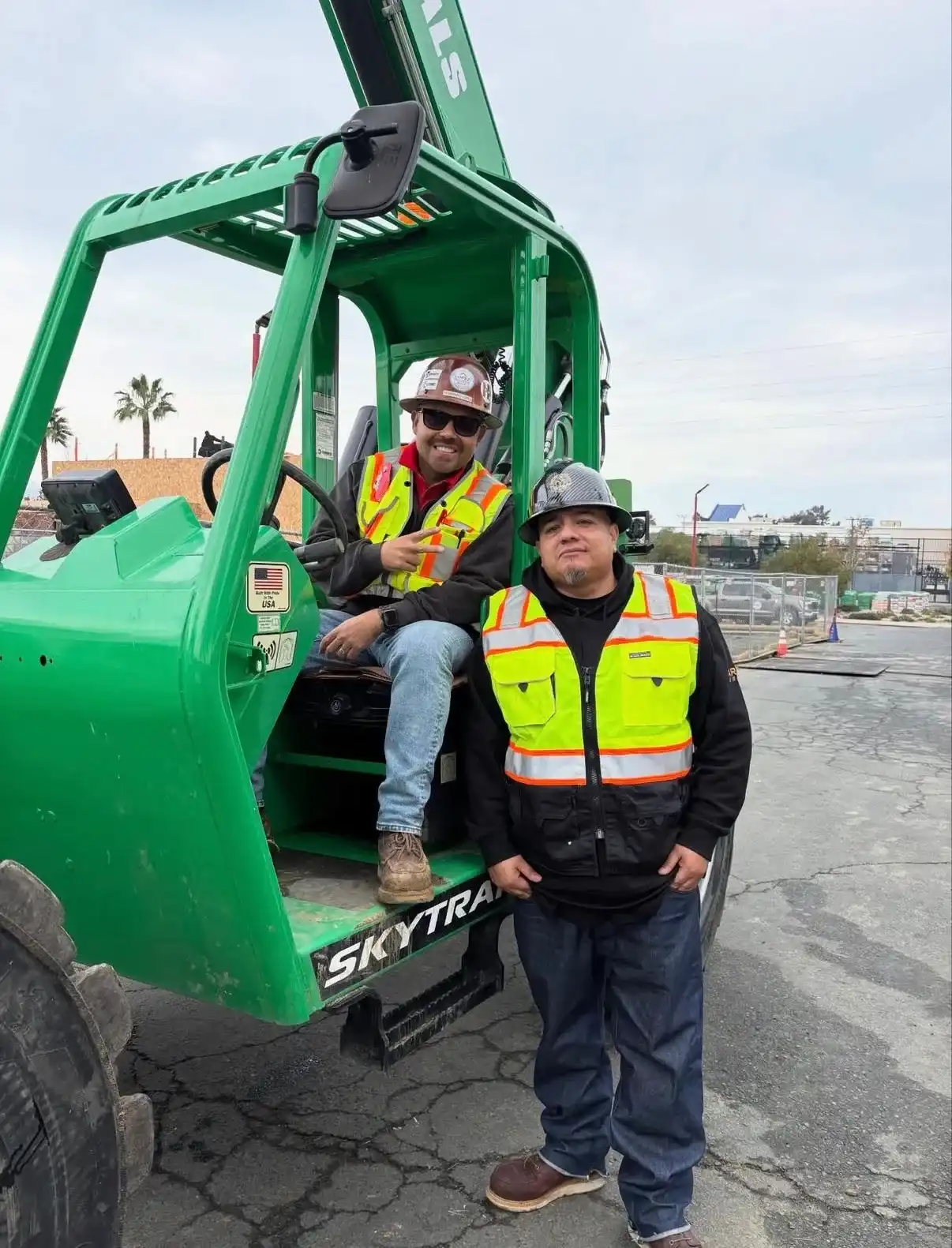 Two Lopez crew members in safety vests with a SkyTrak telehandler on a jobsite